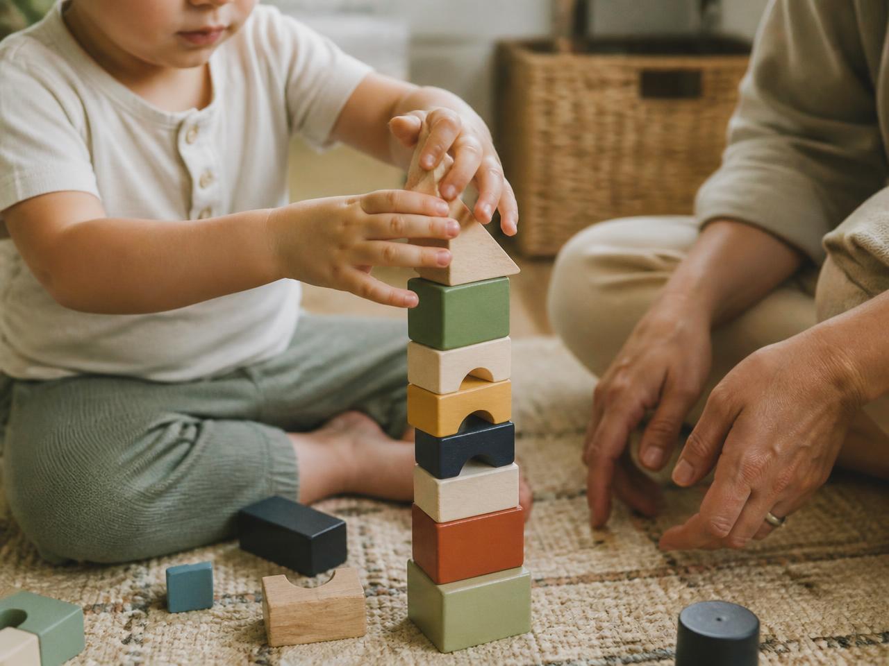 A toddler stacking wooden blocks with a parent nearby